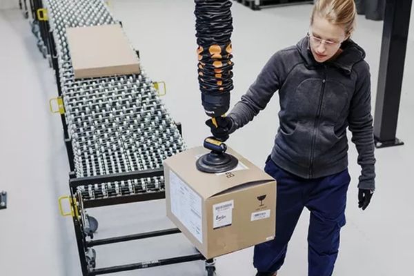 Kransysteme kommen häufig in Logistikzentren zum Einsatz. Eine Frau hebt mit Hilfe eines Krans ein Paket hoch.